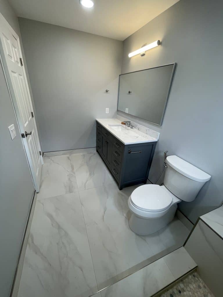 A bathroom with a toilet, sink and mirror undergoing kitchen remodeling.
