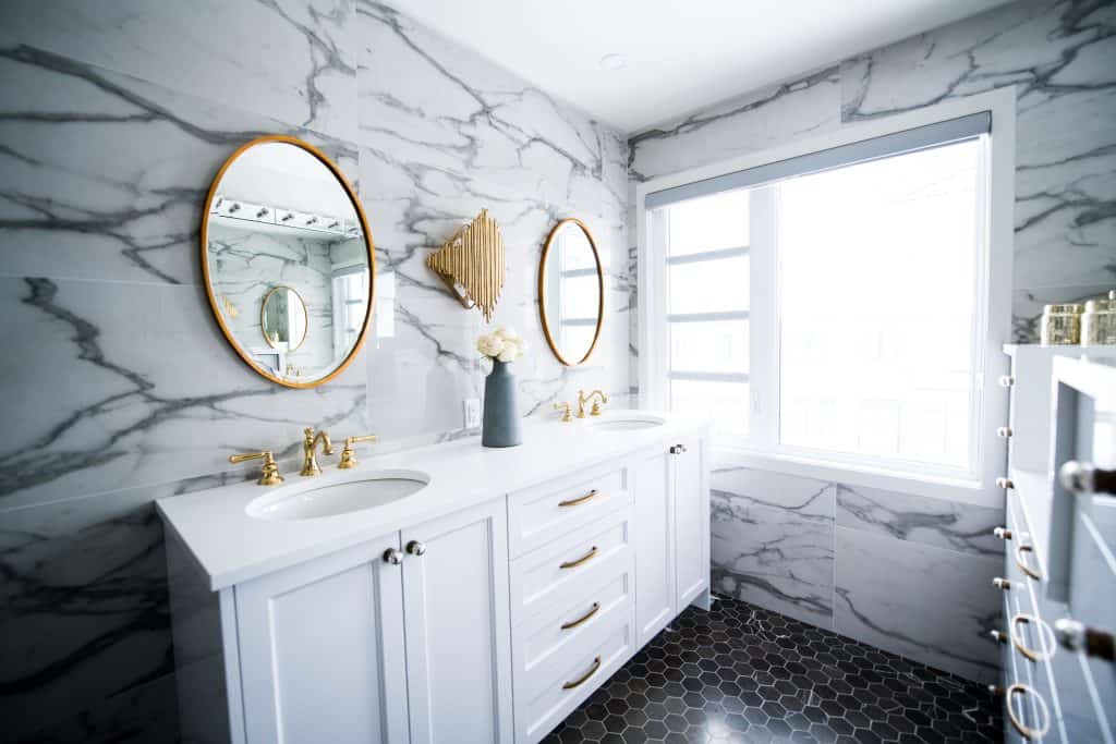 A bathroom with white marble walls and gold mirrors.